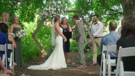 best man hands ring to groom smiling laughing at forest wedding ceremony