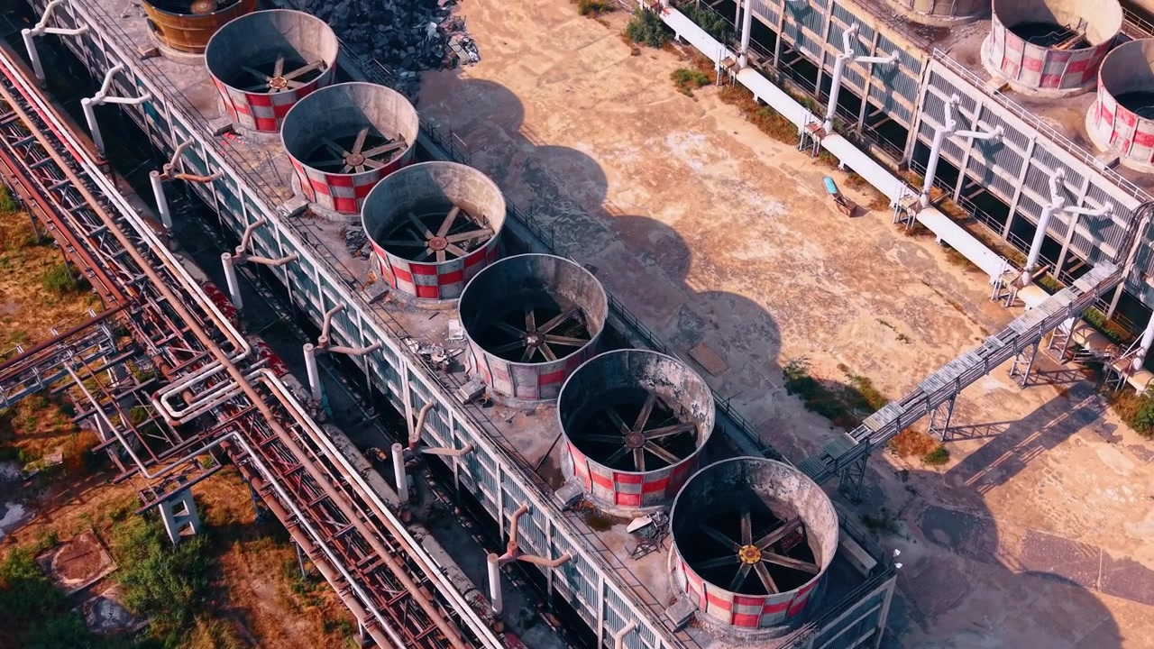 Vista dall'alto di ventole di raffreddamento industriali sul tetto di una struttura. Grandi bocchette di ventilazione rotonde con bordi rossi e bianchi fiancheggiano un edificio in cemento accanto a tubi.