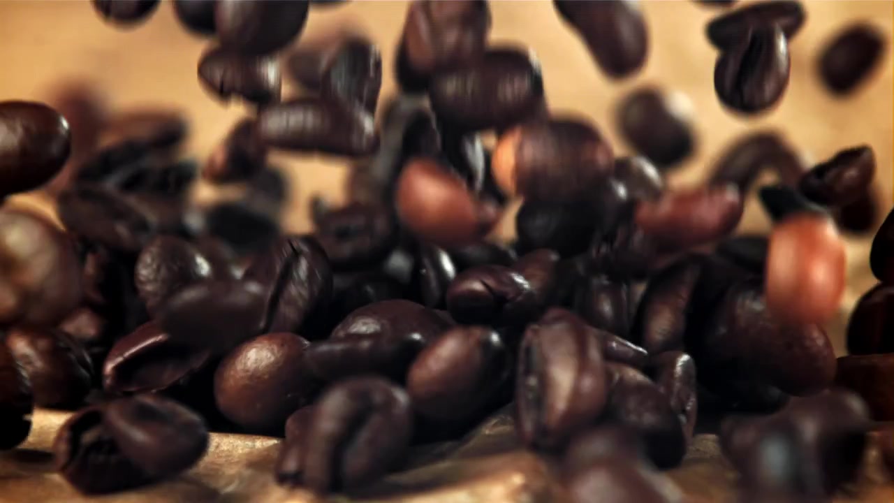 Movimento rallentato di chicchi di caffè tostati che cadono su sfondo marrone
