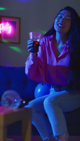 video vertical de mujer borracha sentada en el sofá bebiendo alcohol en la fiesta de la casa 1