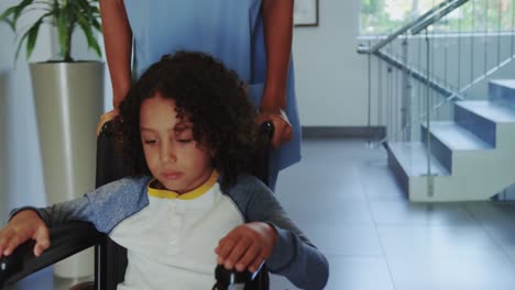 front view of doctor pushing african american boy in wheelchair in hospital corridor 4k