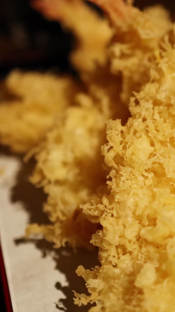Extreme close-up of golden, crispy shrimp tempura with detailed batter texture on a serving tray