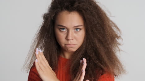 une femme caucasienne aux cheveux bouclés montre un geste d'arrêt.