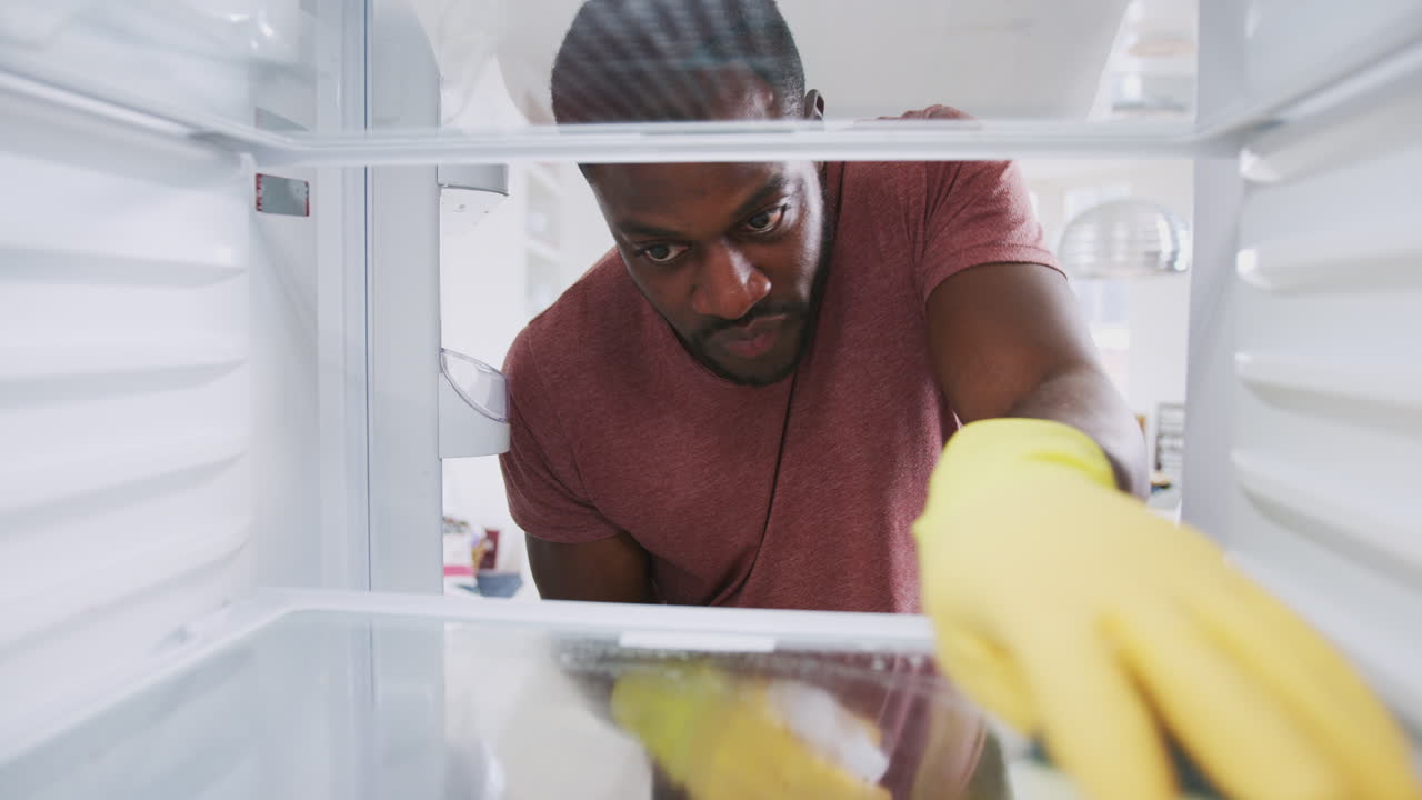 vista mirando desde el interior del refrigerador vacío como hombre con guantes de goma limpia estantes