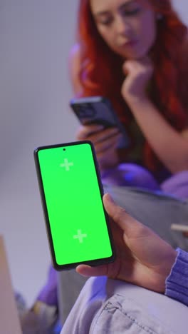 Close-Up-Vertical-Video-Studio-Shot-Of-Young-Gen-Z-Friends-Sitting-On-Sofa-Sharing-Social-Media-Post-On-Green-Screen-Mobile-Phone