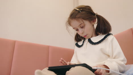 young girl using tablet on a pink couch
