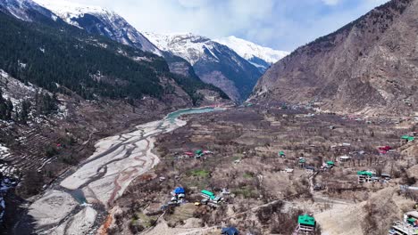 Aerial view of a Himalayan village nestled in a valley with snow-capped mountains.
