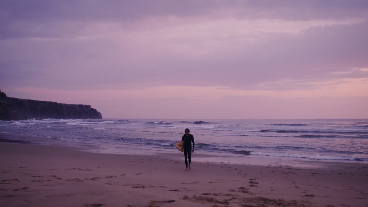 Surfer, der går langs stranden ved solnedgang
