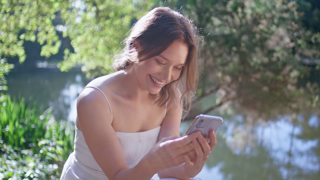 Laughing woman looking smartphone in sunlight river bank closeup. Girl messaging
