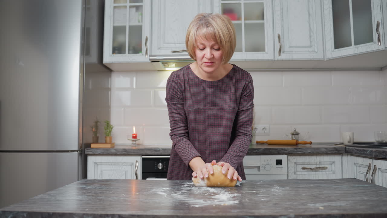 дама выпекает свежее тесто на кухонном столе, готовит домашние выпечки, современная кухня включает в себя катушку, красную свечу, белые шкафы и теплое освещение