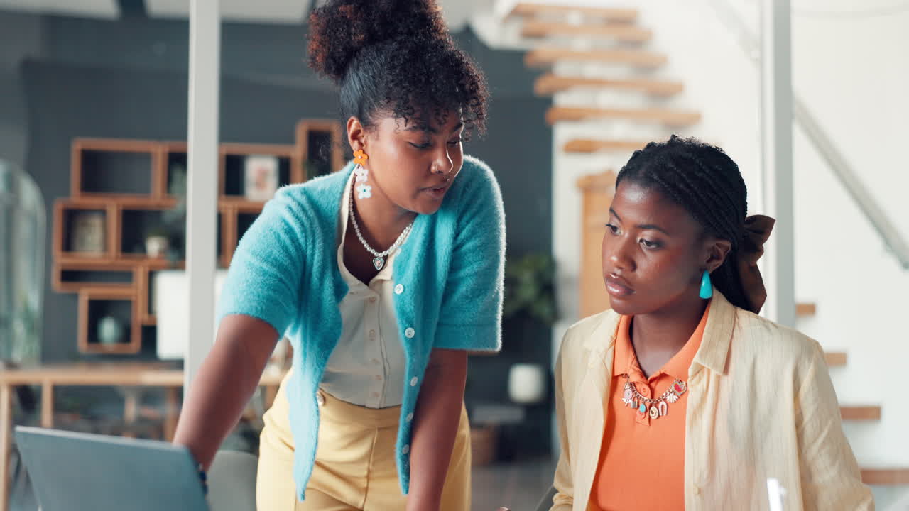 Two Young Businesswomen Collaborating and Discussing Work on a Laptop in an Office