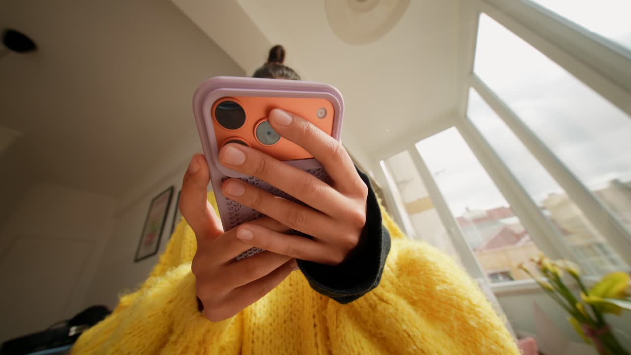 Giovane donna che usa il suo smartphone in casa con disinvoltura.