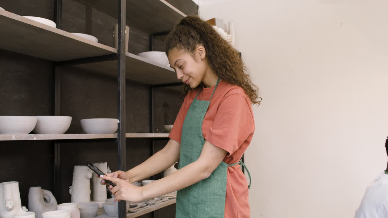 도자기 가게 선반에 있는 수제 도자기 조각 사진을 찍는 여자