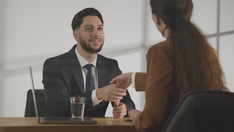 Male-Candidate-Shaking-Hands-With-Female-Interviewer-At-The-End-Of-Job-Interview-Viewed-Through-Window-