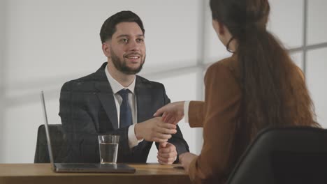 male candidate shaking hands with female interviewer at the end of job interview viewed through window