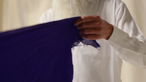 close up studio shot of senior sikh man folding fabric for turban against plain background 2