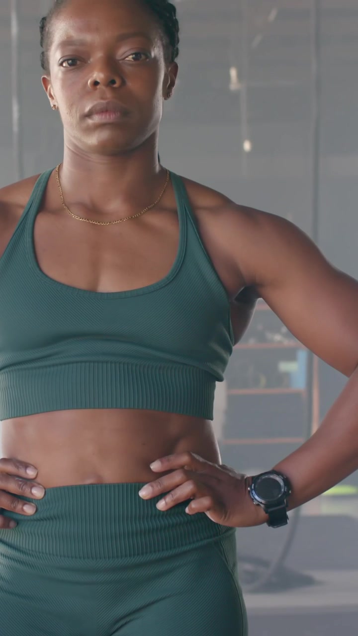 Video verticale: donna afroamericana che posa con le mani sui fianchi mentre la telecamera si alza mostrando la sua forma fisica in palestra.