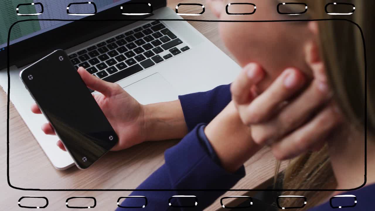 Donna che tiene uno smartphone sopra un laptop e si china, studiando lo schermo per lavoro tecnologico.