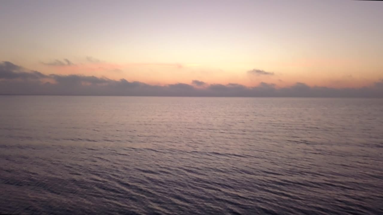 Slow drone flight over calm ocean, sunrise