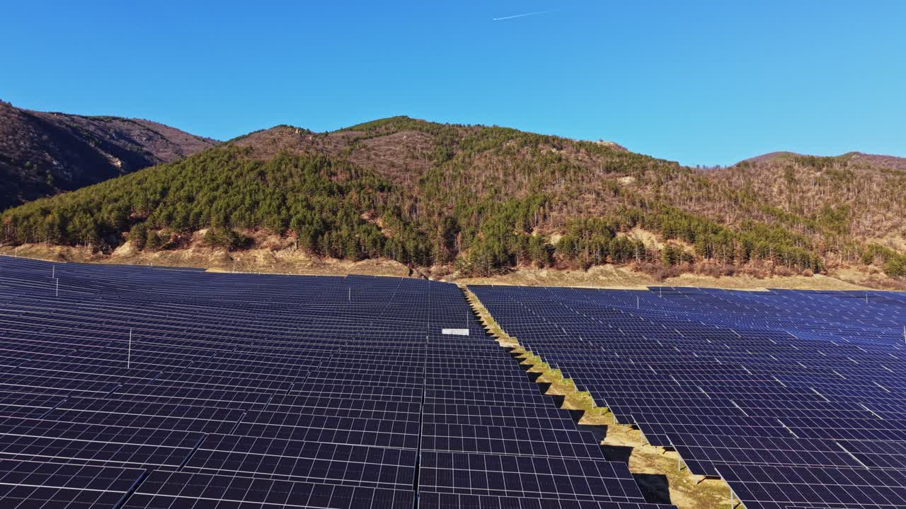 Solpaneler dækker land nær bjerge under en klar, blå himmel
