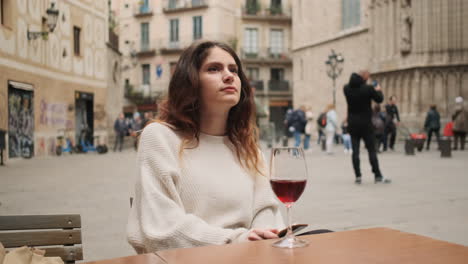 joven mirando a su alrededor mientras está sentada en un café con un vaso de vino rojo