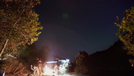 timelapse of camp bonfire with large group of friends gathered around campsite in the evening under the stars in the night sky