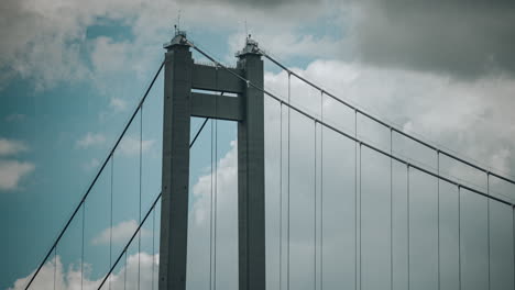timelapse close up shot with the top of a suspended bridge, clouds drifting in the background, hdr