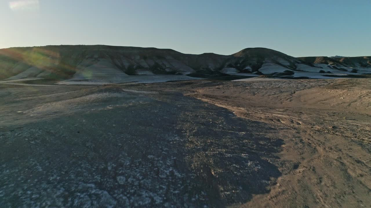 vista aérea rápida y baja que se mueve hacia terraplenes secos y áridos de lutita en un desierto.