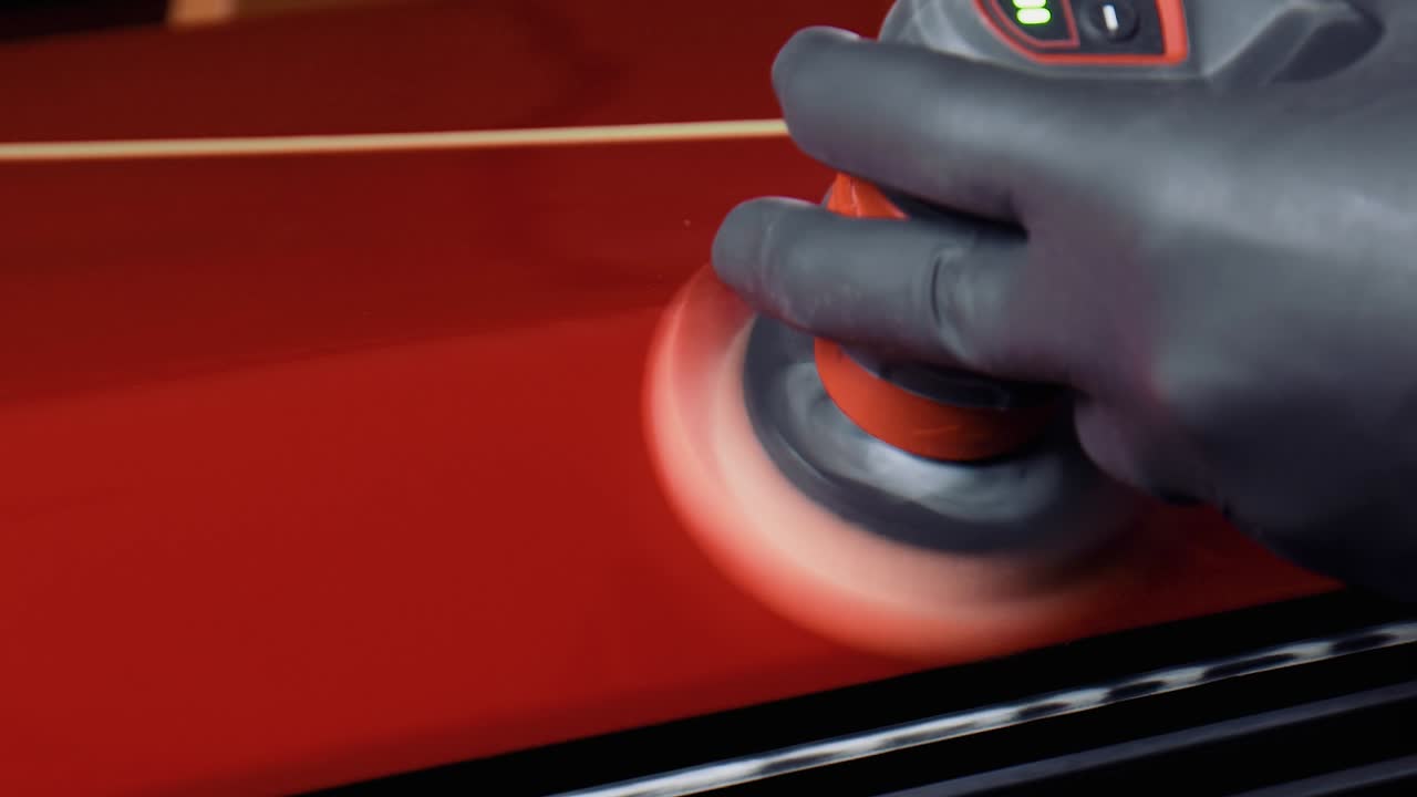 Close-up de um homem com luvas de látex pretas polindo tinta vermelha com uma pequena máquina de polir