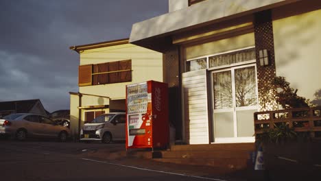 a red coca-cola vending machine outside a building with parked cars on a japanese street