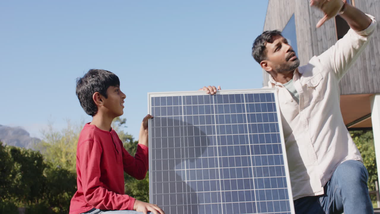 Holding solar panel, Indian father and son discussing renewable energy outdoors