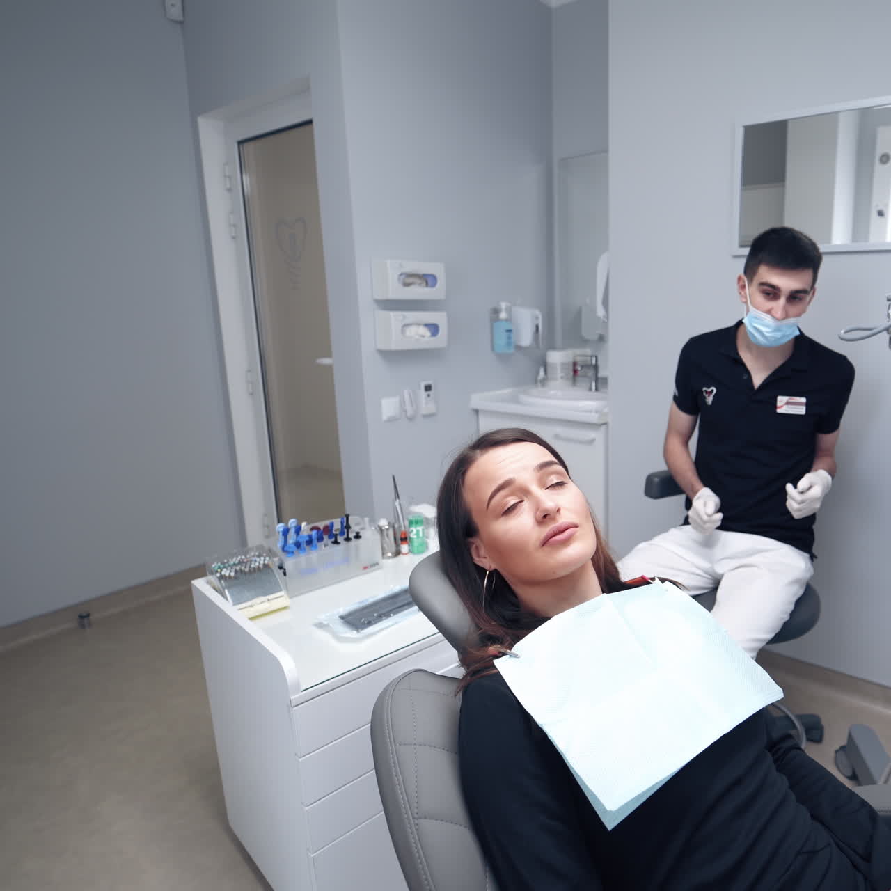 Woman sitting in dental chair. Attractive female visiting stomatologist on modern dental office background. Dentist in mask talks to the patient in clinic.