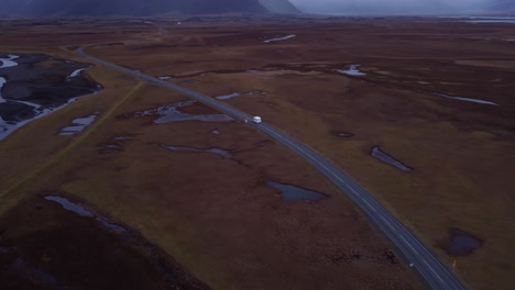 an expansive aerial shot captures a motorhome traveling along a road that cuts through a vast, rugged, and sparsely vegetated icelandic landscape