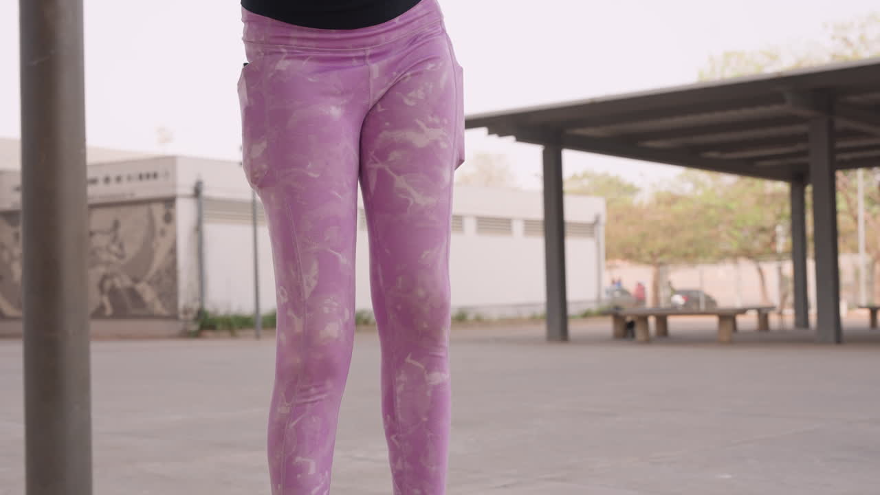 Leggings roxas, aquecimento de dança em praça ao ar livre, close-up das pernas de dançarina urbana praticando passos sob pavilhão, leggings estampadas, tênis casuais no concreto, cena ensolarada com fundo de mural, rítmico.