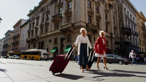two senior women walking with suitcases on a sunny city street