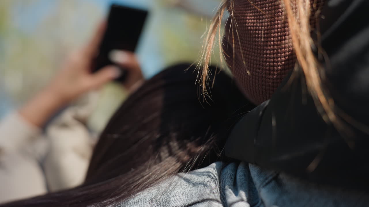 white woman's long hair in closeup foreground while asian friend holds phone in soft focus background, dreamy shallow depth of field park portrait capturing strands, light and subtle social