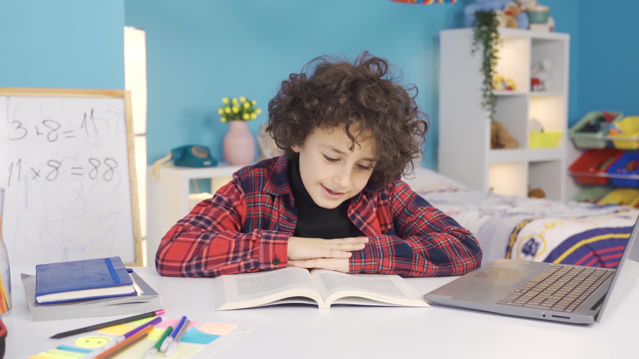 Successful and smart male primary school student reading a book, doing homework.