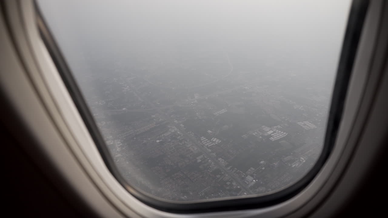 4k dolly shot of the aerial view of the outskirts of Bangkok from a flying plane window with smoke and pollution surrounding the city passenger perspective