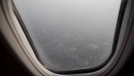 4k dolly shot of the aerial view of the outskirts of bangkok from a flying plane window with smoke and pollution surrounding the city passenger perspective