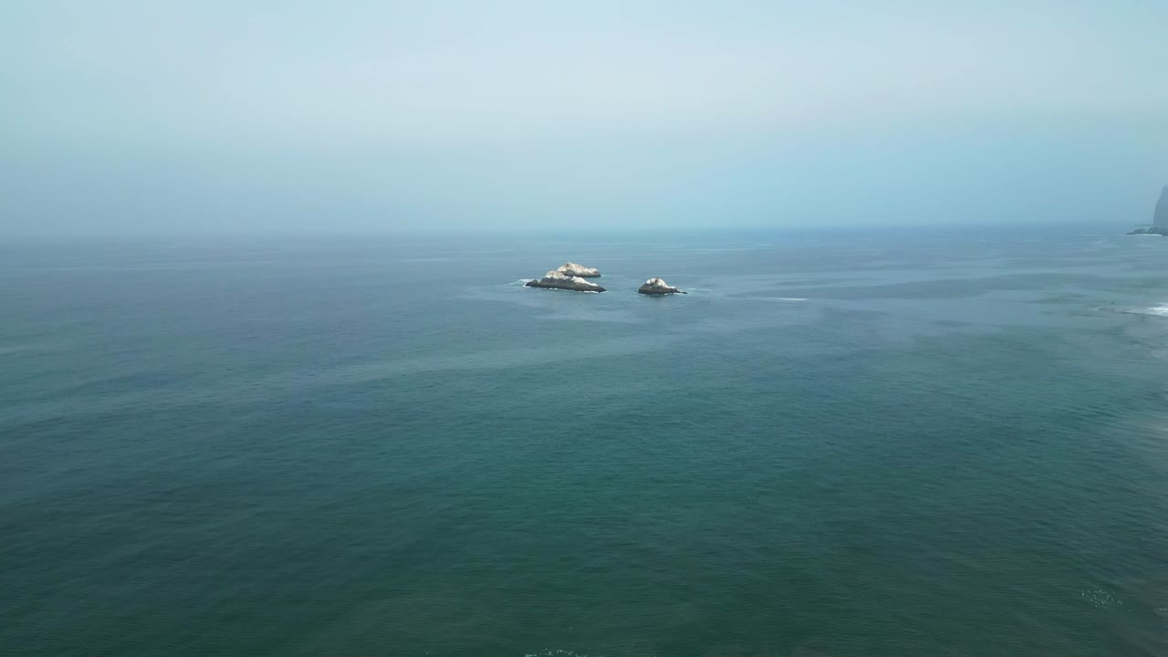 Forward drone shot approaching rocky islands with seabirds off Lima’s coast. Early morning light and clear sky over calm ocean waters.