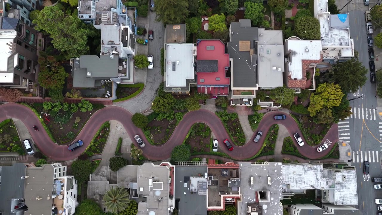 San Franciscon Lombard Street käärmemäisine mutkineen ja tiilipäällysteisine serpentiiniteineen, autot ajavat hiusneulamutkia puutarhaistutusten ohi suoraan ylhäältä nähtynä. Kalifornia, USA. Ilmakuva ylhäältä alaspäin nouseva.