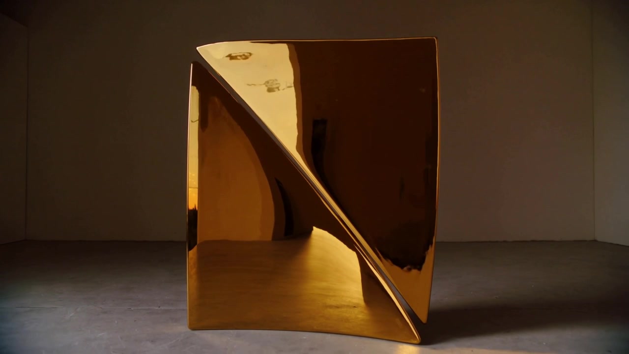 Scultura in oro lucido riflettente che rivela una piega diagonale mentre la telecamera panoramica si muove attraverso la galleria.