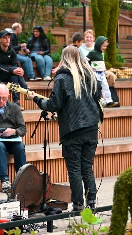 woman playing acoustic guitar on stage in city park