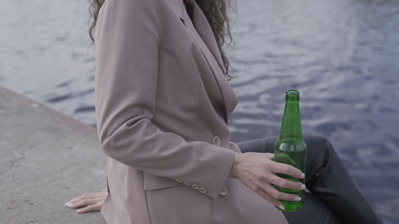mujer morena rizada feliz hablando con su amiga y bebiendo cerveza en la orilla del río