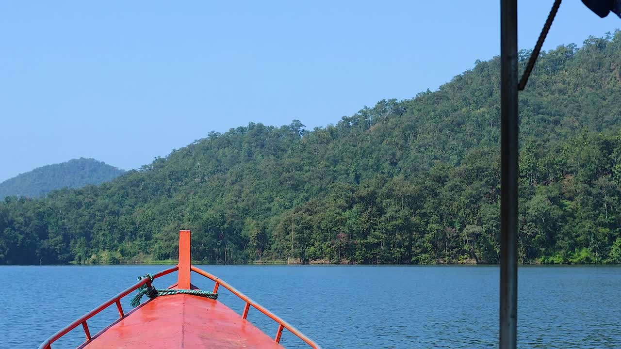 A boat's bow points towards verdant hills under a clear blue sky, with calm lake waters.