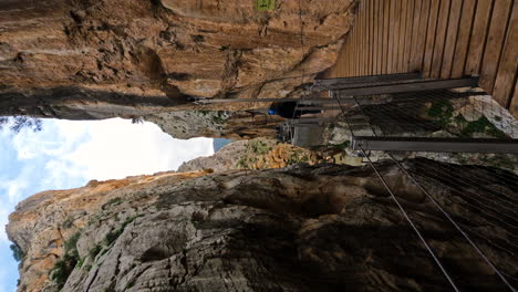 4k-Vertical-shot-of-tourists-walking-on-a-wooden-bridge-at-El-Caminito-del-Rey-in-Gorge-Chorro,-Malaga-province,-Spain