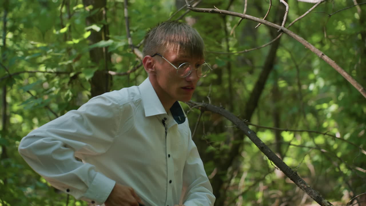 Young scientific researcher carrying backpack walking carefully through thick green forest under sunlight, moving cautiously among trees and foliage with natural atmosphere of wilderness exploration