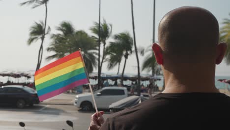 man holding pride flag at beach