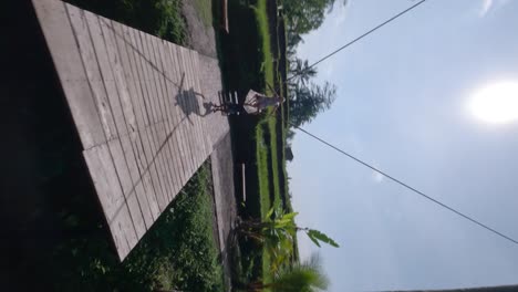 Vertical-FPV-Rotating-shot-of-a-beautiful-lady-swinging-on-a-swing-set-in-the-tropical-nature-in-a-large-dress