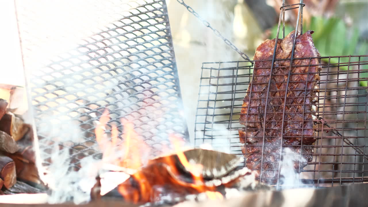 Wood fire burning and juicy lamb rib on grid being grilled upright, telephoto